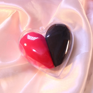 Red and black heart-shaped makeup sponge set in clear case on pink silk fabric