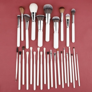 Detail view of 32 professional makeup brushes with white handles on a red leather surface