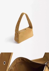 Detail view of mustard suede shoulder bag featuring silver metal eyelets and zipper closure