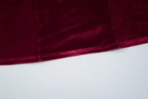 Detailed close-up of soft burgundy velvet fabric texture and hemline of the dress