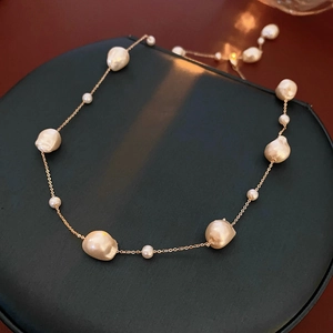 Macro detail of gold plated necklace with irregular baroque pearls on a green cushion