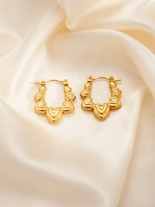 Detailed macro view of golden heart-shaped hoop earrings on elegant cream satin fabric