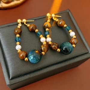 Détail de boucles d'oreilles en œil de tigre et perle sur un écrin noir avec soleil