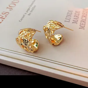 Irregular textured gold C-shape stud earrings with lava pleat design on vintage book