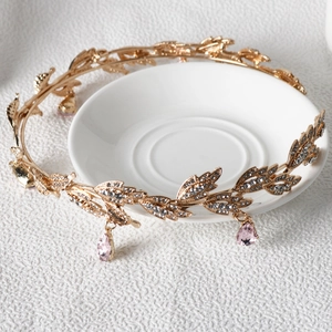Detailed view of a gold leaf bridal crown with pink teardrop crystal on a white plate