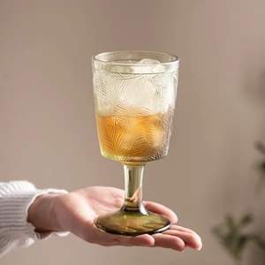 Green embossed vintage glass goblet with leaf patterns held against a soft background