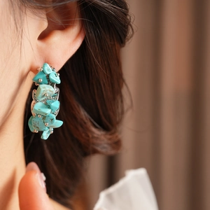 Détail de boucles d'oreilles en C avec pierres turquoise concassées sur métal argenté