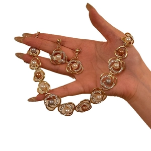Elegante conjunto de joyas florales doradas con perlas y diamantes en mano sobre fondo blanco