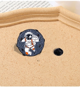 Detailed close-up of a creative round astronaut enamel pin with metal clutch on sandy texture