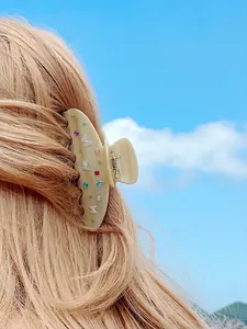 Pinza per capelli a farfalla beige con strass colorati su modella e sfondo del cielo
