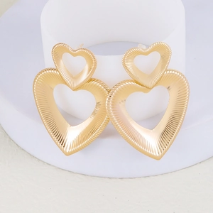 Close-up of golden double heart drop earrings with a detailed radial striped texture finish