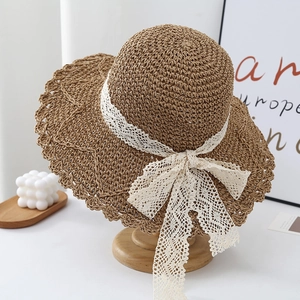 Detailed view of brown straw hat featuring white lace bow and elegant wavy brim