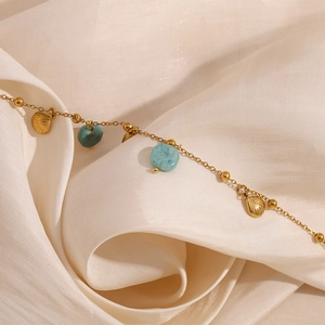 Detail of 18K gold-plated anklet with shell pendant and turquoise stone on silk