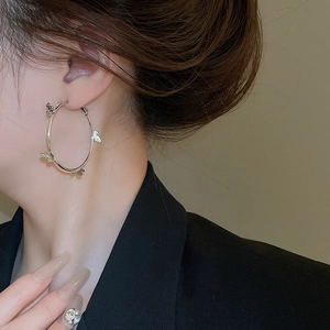 Close-up of a large silver hoop earring with delicate butterfly accents on a female model