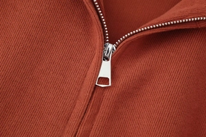 Detailaufnahme von Metallreißverschluss und Rippstrickgewebe an einem rostroten Hoodie