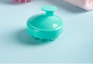 Close-up of a green silicone scalp massager brush with ergonomic grip on blue background