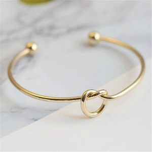 Macro shot of minimalist gold knot cuff bracelet with ball ends on marble background