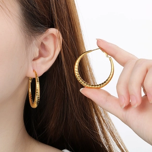 Detailed view of large gold striped hoop earrings showing size and texture on a model
