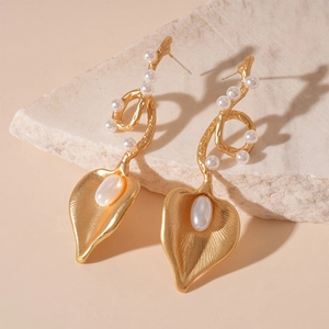 Detailed shot of golden branch earrings featuring textured leaves and white faux pearls
