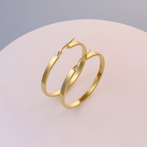 Macro detail of large gold flat-wire hoop earrings on a minimalist display stand