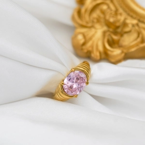 Detail of a gold plated ring featuring a large pink oval gemstone on white silk