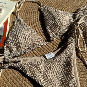 Flat lay of cream crochet bikini with metal ring details and washing instruction label