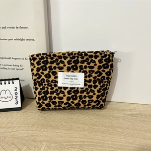 Close-up of leopard print corduroy makeup pouch with metal zipper on a wooden table