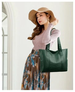Detail of large dark green PU leather tote bag held by a model in a casual outfit