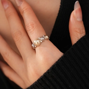Detailed close-up of a pearl ring with zircons and gold-toned pearls on finger
