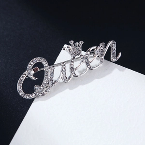 Vue détaillée d'une broche Queen argentée avec couronne et cristaux sur fond bicolore
