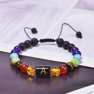 Macro detail of hand-woven chakra bracelet featuring volcanic lava beads and golden letter A
