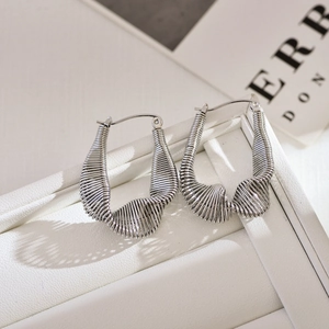 Silver twisted wire hoop earrings with irregular U-shape design on white leather