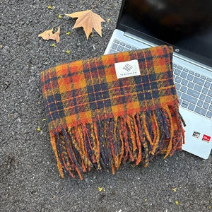 Orange and navy blue plaid mohair scarf with fringes and brand label on autumn leaves