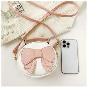 Mini round white crossbody bag with pink bow on knit fabric, size shown next to a phone