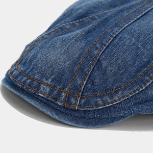 Macro shot of blue denim flat cap with vintage contrast stitching and twill fabric texture