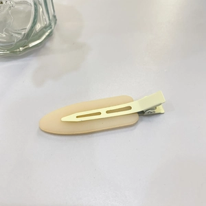 Detail view of a cream matte duckbill hair clip with a smooth oval finish and metal spring