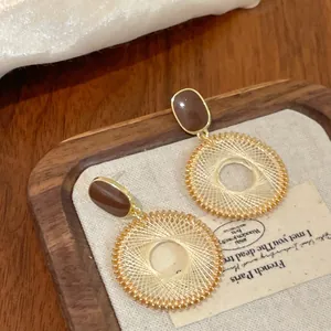 Détail de boucles d'oreilles bohèmes tissées avec pierre brune et bordure dorée