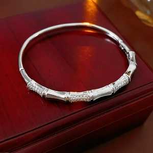 Macro shot of silver bamboo-style bangle with inlaid zircons on a dark wood box