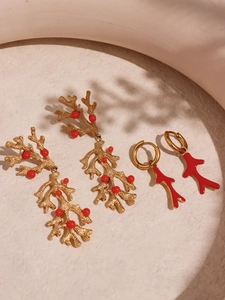 Detail view of 18k gold plated coral earrings with red beads on a textured surface