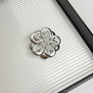 Macro shot of silver camellia flower brooch with hollow metal petals on textured surface