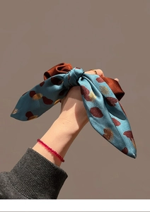 Detail of silk satin scrunchie with blue and brown bow pattern held in hand
