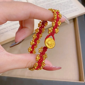 Detail eines roten geflochtenen Armbands mit Goldmünze über einem Buch gehalten