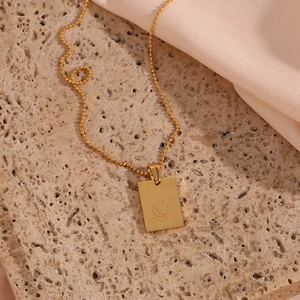 Macro detail of a gold rectangular pendant with moon and star engraving on a bead chain