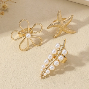 Gold ocean style ring set with flower, starfish and white pearls on warm beige surface