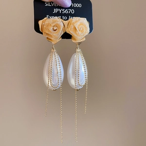 Macro detail of fabric rose earrings with teardrop pearls and long golden chain tassels