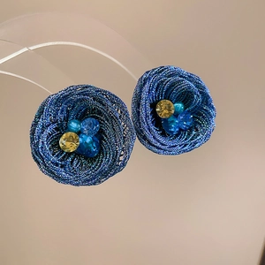 Close-up of blue hand-woven flower earrings with yellow beads and detailed spiral texture