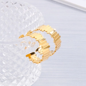 Détail de boucles d'oreilles créoles dorées en C avec bords ondulés sur verre