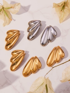 Detailed close-up of gold and silver wing-shaped stud earrings on a marble surface