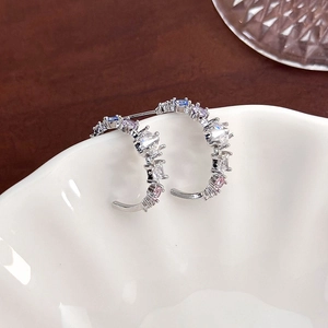 Detailed close-up of C-shaped earrings with colorful gemstones on a white ceramic bowl