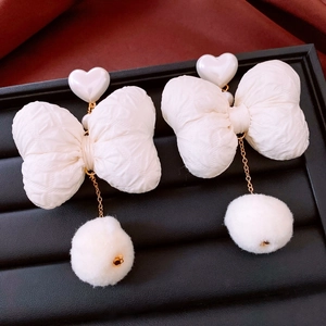 Detail of white fabric bow earrings with heart studs and soft plush pompom pendant